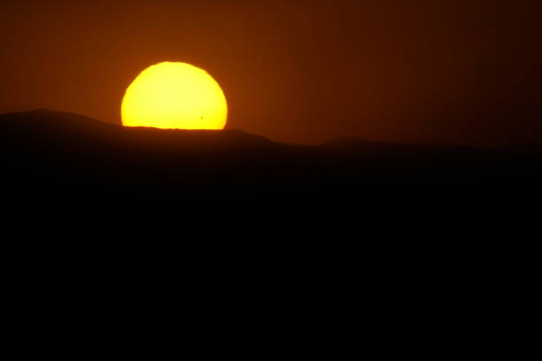 The photos show the sunset in Rassudr, Egypt over the rugged mountains as the sun slowly disappears behind the peaks. The mountains in the background give the images a three-dimensional feel. The silhouetted mountains create a dramatic contrast against the fading light, while the peaceful atmosphere captures the beauty of nature at dusk.