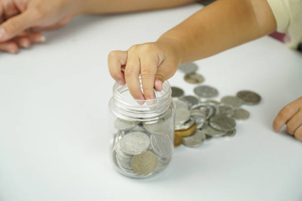 istock Child Depositing Coins in Savings Jar 2198655841
