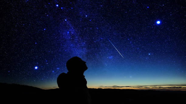 istock Silhouette of a man observing Milky Way stars, planets and other celestial objects from a dark countryside location. 2198656438
