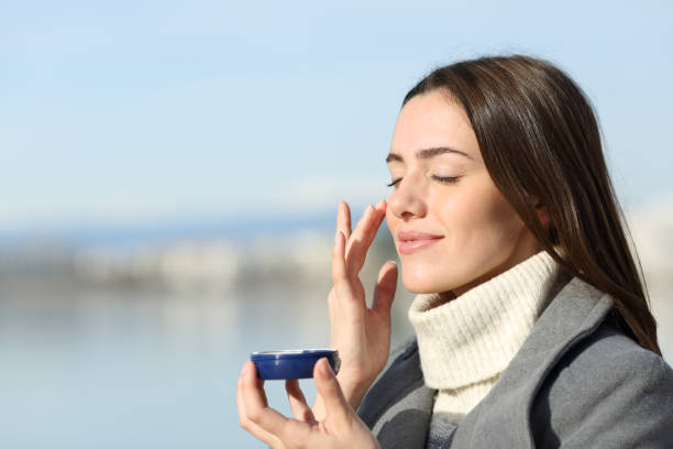 Satisfied beautiful woman in winter applying moisturizer cream stock photo