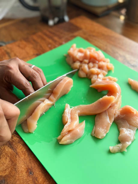 istock Image of unrecognisable person slicing raw chicken breast on plastic chopping board in domestic kitchen, man holding sharp knife slicing meat, wooden kitchen counter, elevated view, focus on foreground 2198667675