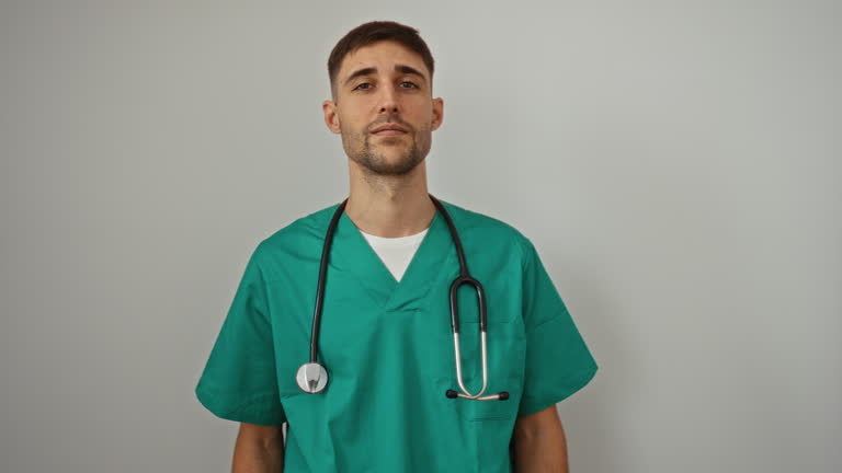 Handsome young man in green scrubs with stethoscope over white background portrays a confident healthcare professional.