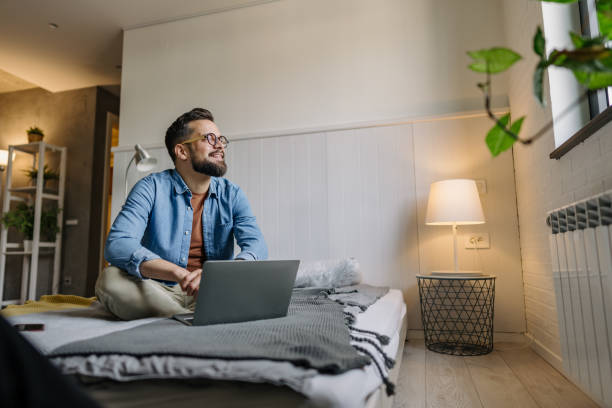 Young man working from home sitting on bed using laptop