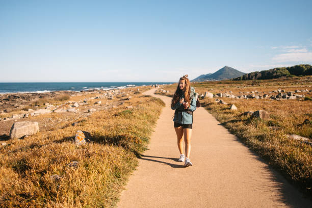 Camino de Santiago – Portuguese Way. A woman with a backpack walking on the Camino on a sunny day and eating an acai smoothie. Alternative ways of life. Backpacker walking