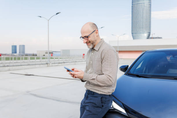 istock Smiling businessman checking phone while leaning on the car in rooftop parking 2198683472
