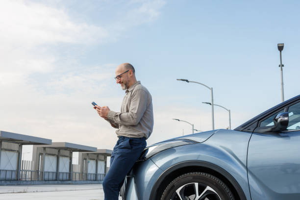 Modern businessman using smart phone near car in open parking lot