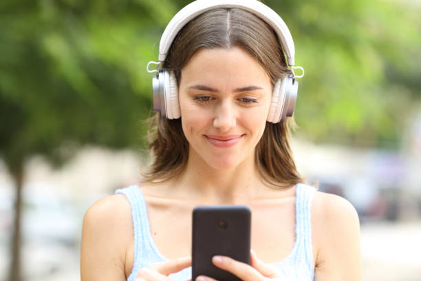 istock Satisfied woman wearing headphone using phone in a park 2198684413