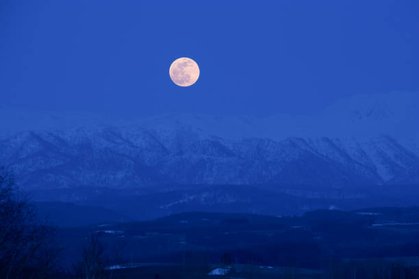 Full moon rising from the snowy mountains in spring