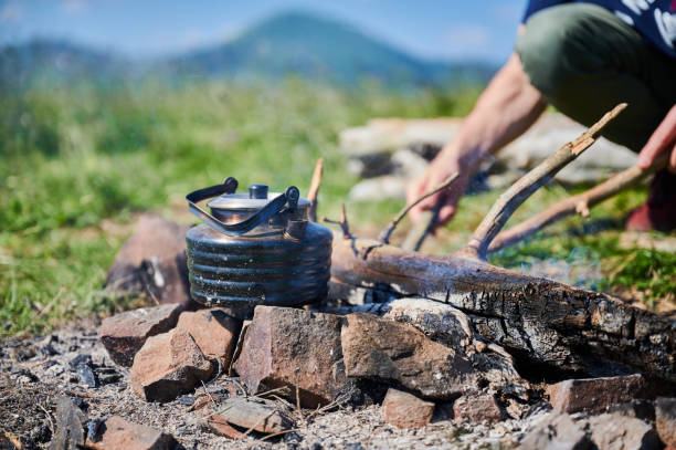 Close-up of blackened kettle heating over campfire, surrounded by stones.