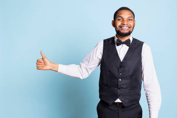 istock Smiling bellboy in suit and tie showing thumbs up gesture in studio 2198690415