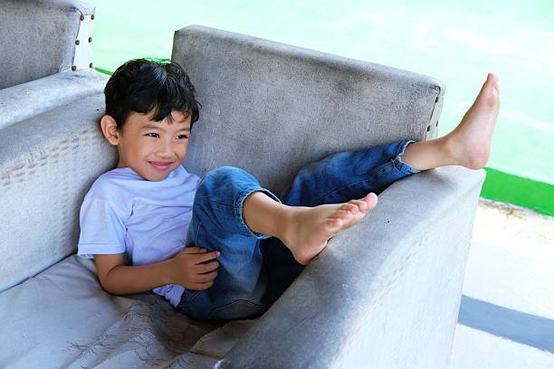 istock A cheerful young boy in a white t-shirt and jeans laughs joyfully while reclining on a worn-out couch. 2198692142