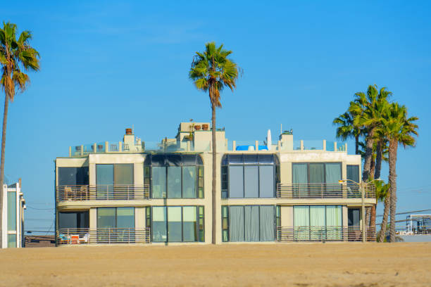 Los Angeles, California - December 18, 2024: Stylish oceanfront building featuring large windows and balconies surrounded by palm trees near Venice, California, under a clear blue sky.