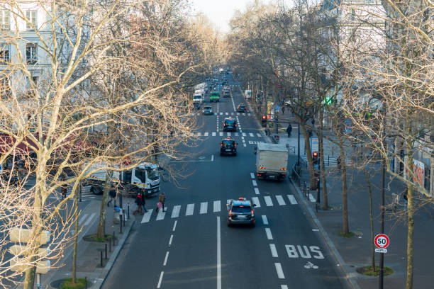 Paris,France-14.01.2025 Traffic flows along a city street lined with bare trees, as pedestrians navigate crosswalks under clear skies on a winter day.