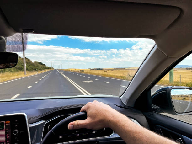 istock A wide-angle view through a car’s windscreen reveals a highway through a desert plain, framed by the interior, steering wheel, and driver’s hands under a clear blue sky with fluffy clouds 2198702761