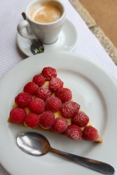A slice of French raspberry tart made with rich pastry cream and fresh berries, served with an espresso coffee.