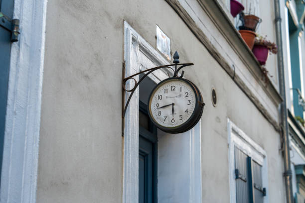 Paris,France-14.01.2025 A vintage clock is elegantly mounted on the exterior of a building, showcasing its classic design amidst colorful flower pots and charming architecture in the neighborhood.