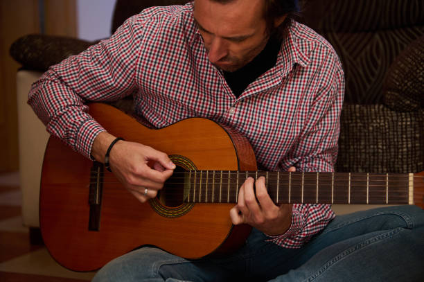 istock Man playing acoustic guitar while sitting indoors in a relaxed atmosphere 2198707616