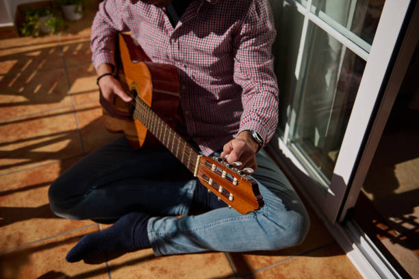 istock Person tuning an acoustic guitar while sitting on a sunlit tiled floor 2198707647