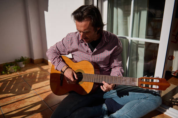 istock Man playing an acoustic guitar in a sunlit indoor balcony space 2198707652
