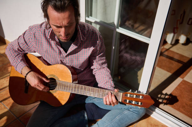 istock Man Playing Acoustic Guitar While Sitting in the Sunlight Indoors 2198707654