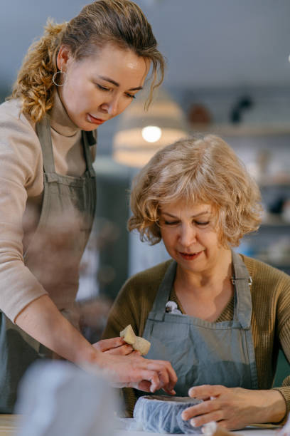 istock Teacher helping retired woman shape ceramic piece at indoor pottery class 2198709929