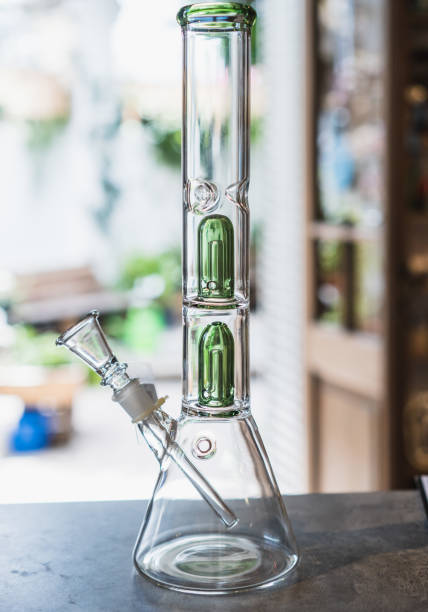 istock A clear glass bong with a cylindrical base and flared mouthpiece sits centered on a rustic wooden surface. 2198710433