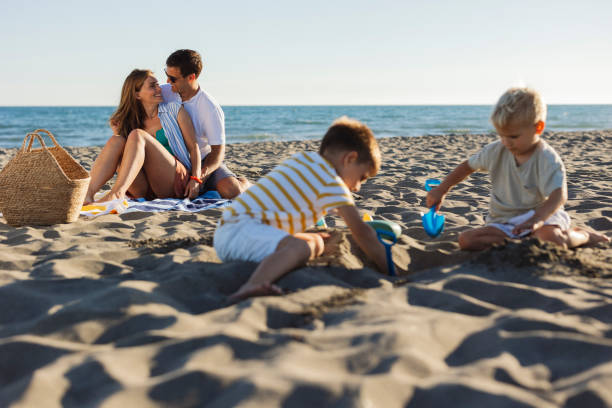 istock Happy family enjoying beach vacation while children playing with sand 2198712748
