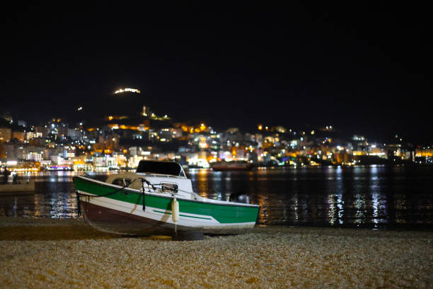 small fishing boat of white and green color on the shallows of the sea bay in the night city of Saranda in Albania