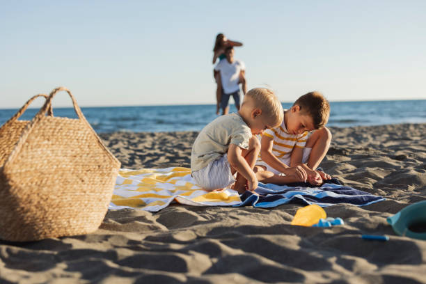 istock Two young brothers playing on the beach while parents watch from afar 2198712912