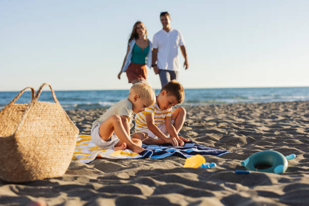 istock Two young brothers playing on the beach while parents walking in blurred background 2198712986