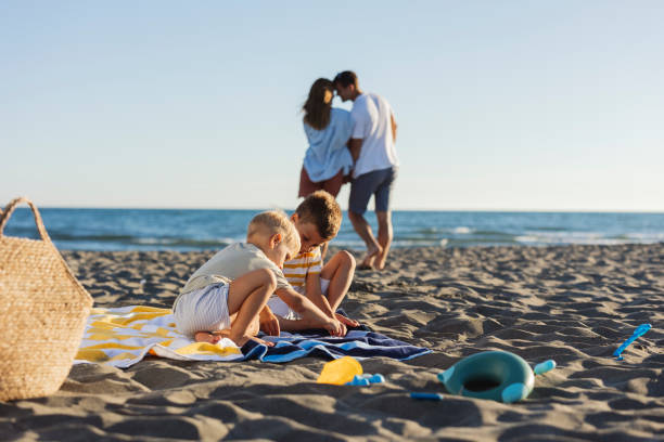 istock Two young brothers playing on the beach while parents relax in the background 2198712990