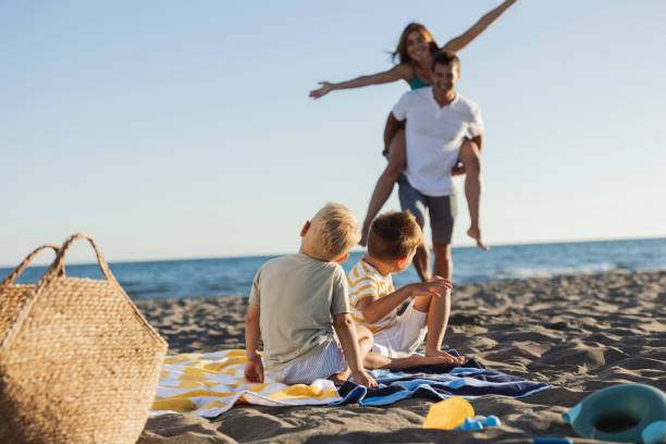 istock Two young children watching their parents playing on the beach 2198713018