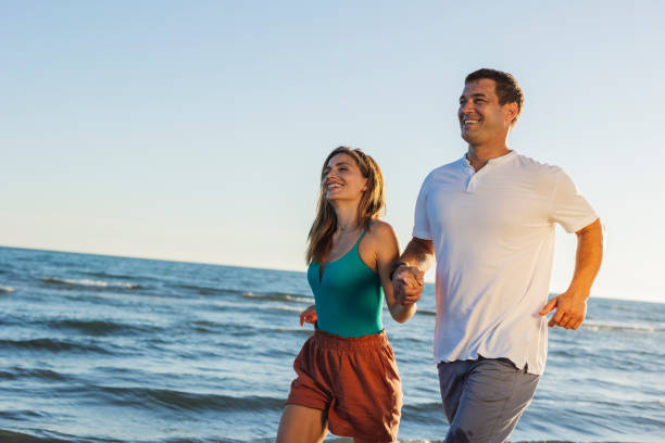 istock Happy couple running on the beach at sunset 2198714378