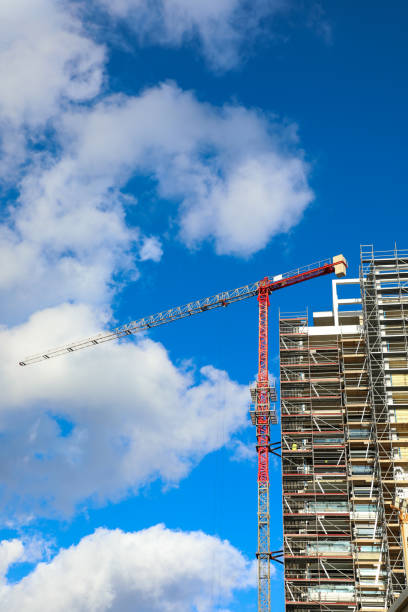 istock Construction of high rise building using tower crane and scaffolding against blue sky and clouds. 2198716144