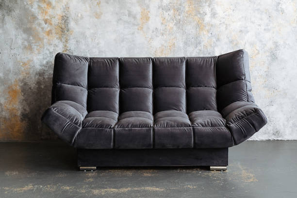 A stylish black couch positioned in front of a raw concrete wall creates a striking and eyecatching visual contrast, enhancing the overall aesthetic appeal and ambiance of the space
