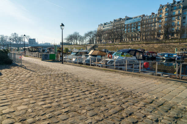 Paris,France-14.01.2025 A scenic riverside pathway lined with cobblestones and moored boats, bathed in sunlight, allows visitors to enjoy a peaceful day outdoors amidst urban architecture.