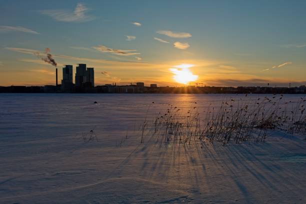 Silhouette of city buildings during sunset in winter with sea frozen in foreground, Kivinokka, Helsinki, Finland.