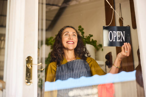 Mature woman turning open sign on small business door stock photo