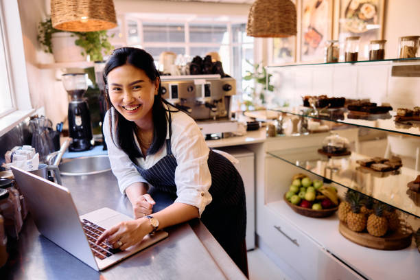 istock Cheerful cafe worker using laptop on counter top, smiling towards camera 2198722941