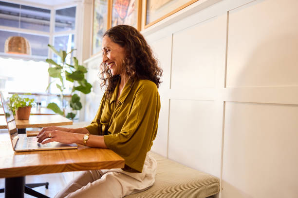istock Mature woman sitting in cafe using laptop, smiling, side view 2198723565