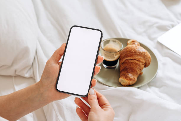 istock Mock up women's hand holding using smartphone with white blank screen at home in bed during breakfast, mobile app design and advertising, online marketing 2198725939