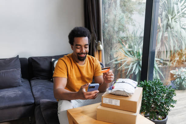 istock Man smiling while shopping online with smartphone and credit card at home 2198726007