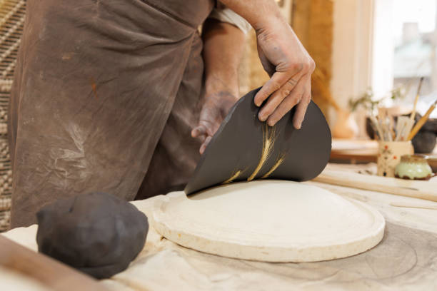 Cropped shot of craftsman forming black clay plate in studio