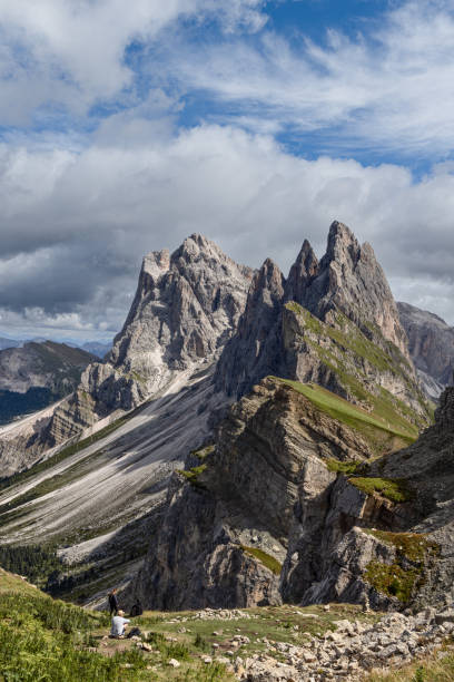 istock Hikers on green slopes of Seceda Ridge, Dolomites, surrounded by rugged peaks, rocky cliffs, and clouds in an alpine setting 2198727607
