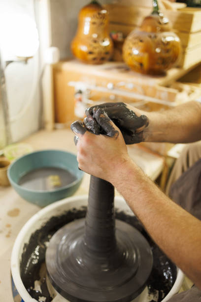Partial shot of potter shaping black clay on pottery wheel in blurred workshop