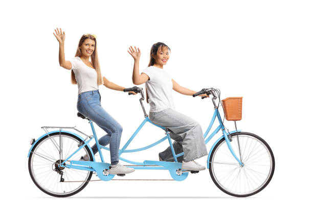 istock Young women riding a tandem bicycle and waving 2198741253