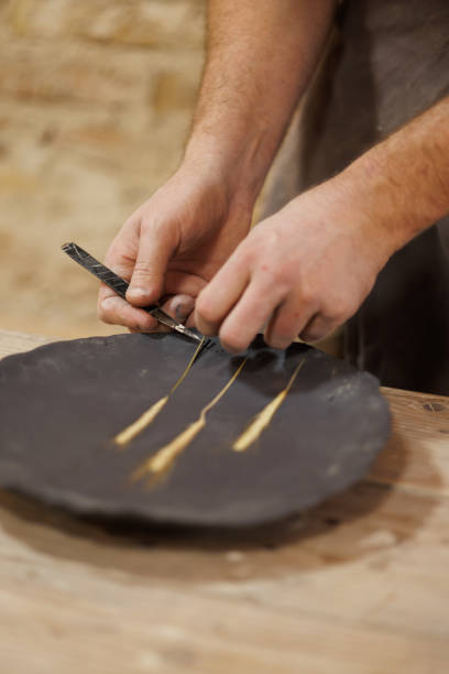 istock Part of craftsman cutting wheat spikelet while making embossing on earthenware in studio 2198742686