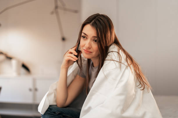 istock Young woman talking on smartphone while sitting on comfortable bed 2198748470