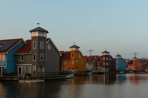 Vibrant modern houses with unique tower-like structures lining a peaceful canal, reflecting warm hues of the evening light. A striking example of contemporary Dutch waterfront architecture. Captured in Groningen, Netherlands, Europe.