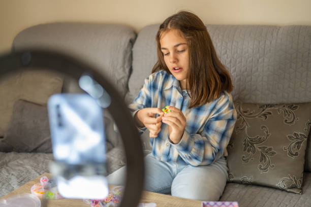 istock Concentrated young girl sitting on a comfortable sofa, recording a diy tutorial with her smartphone and a ring light, engaging with her online audience by crafting colorful objects 2198753977